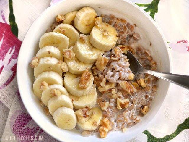 A bowl of Banana Nut Breakfast Farro topped with sliced bananas and walnuts, a spoon in the center