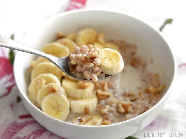 Side view of a bowl of Banana Nut Breakfast Farro with a spoon lifting a bite toward the camera