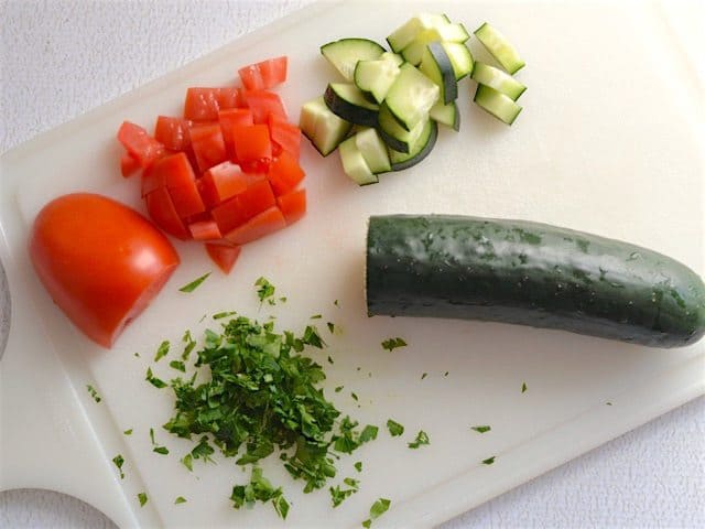 Chopped tomato cucumber, and parsley on a cutting board