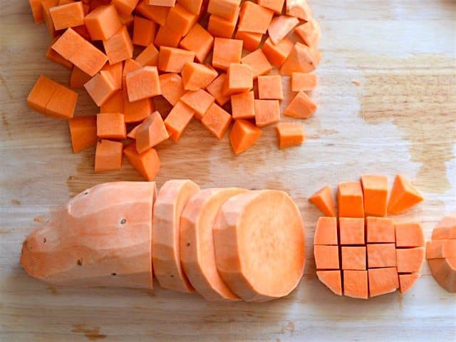Peeled and cubed sweet potatoes on a wooden cutting board