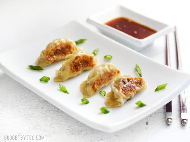 four Pork Gyoza on a rectangular white ceramic plate next to a small dish of soy sauce.