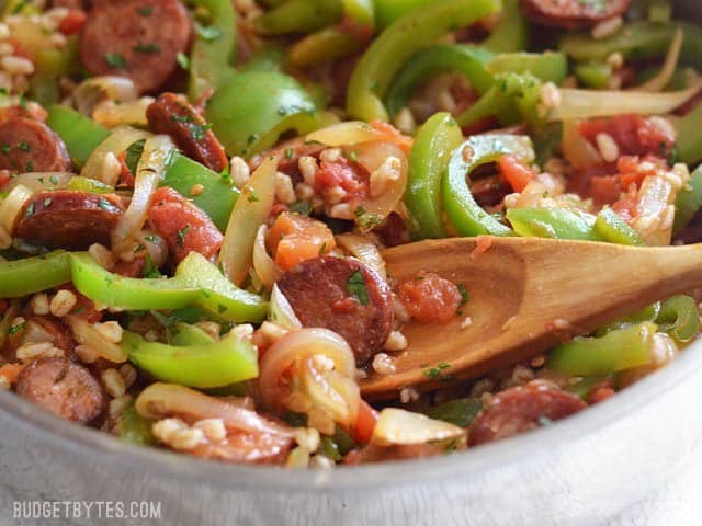 Close up of smoked sausage with peppers and farro in the skillet with a wooden spoon