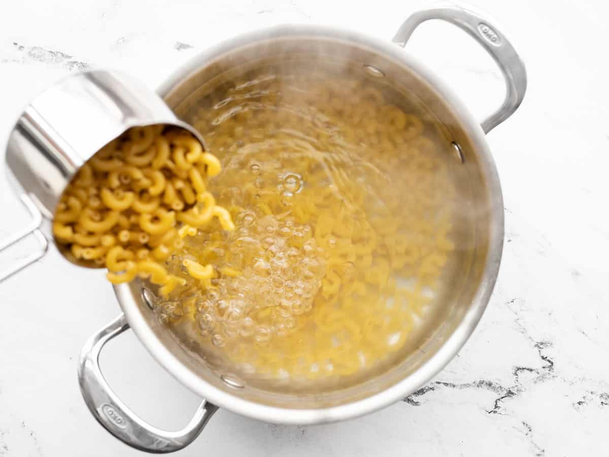 Macaroni being poured into a pot of boiling water
