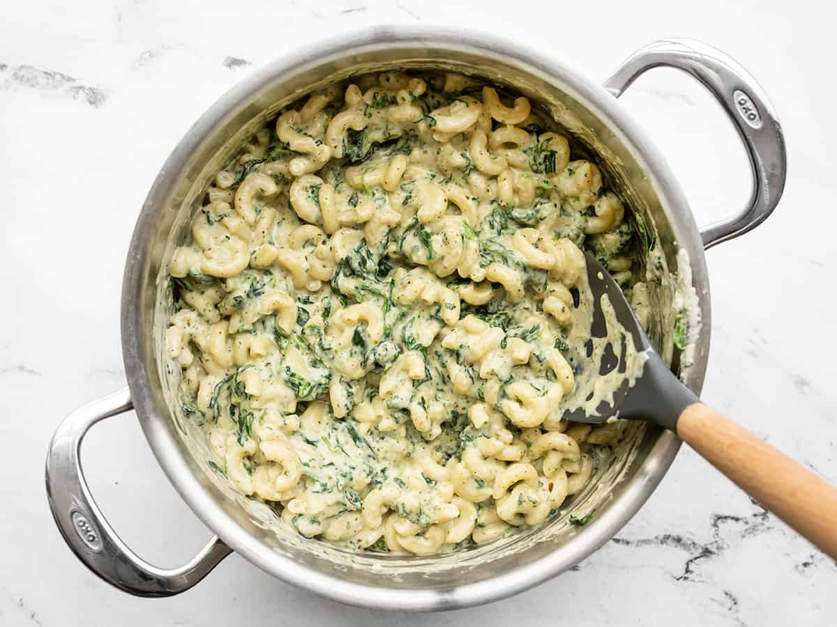 Finished creamy pesto mac in a pot with a large spoon