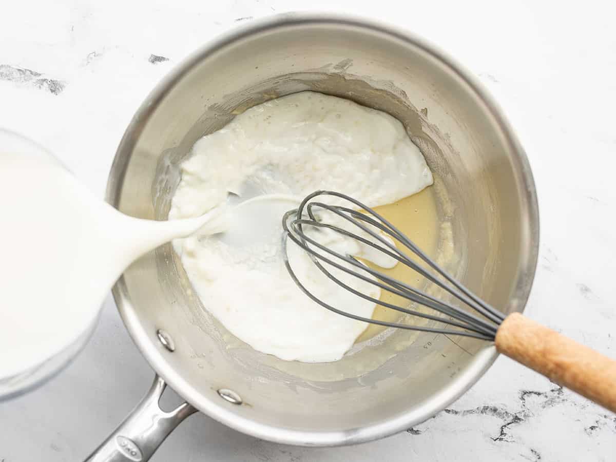 Milk being poured into the sauce pot with the roux