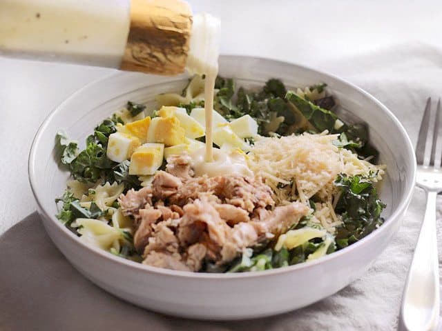 Caesar dressing being poured over the bowl of salad