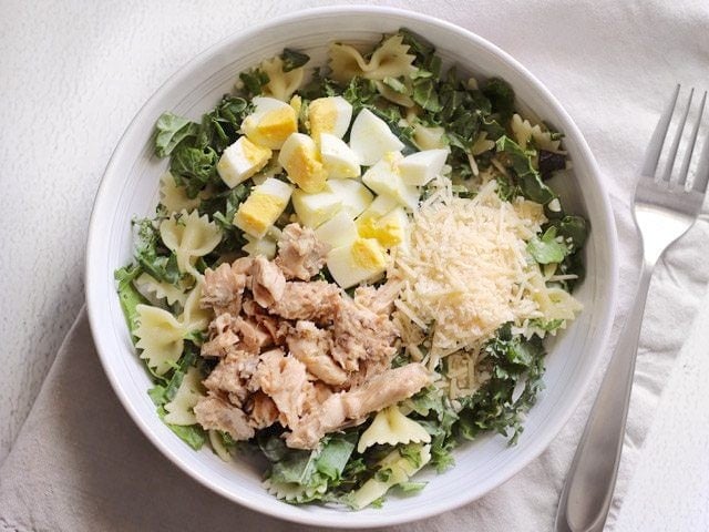 Kale and pasta in a bowl, topped with chopped egg, shredded parmesan and salmon pieces