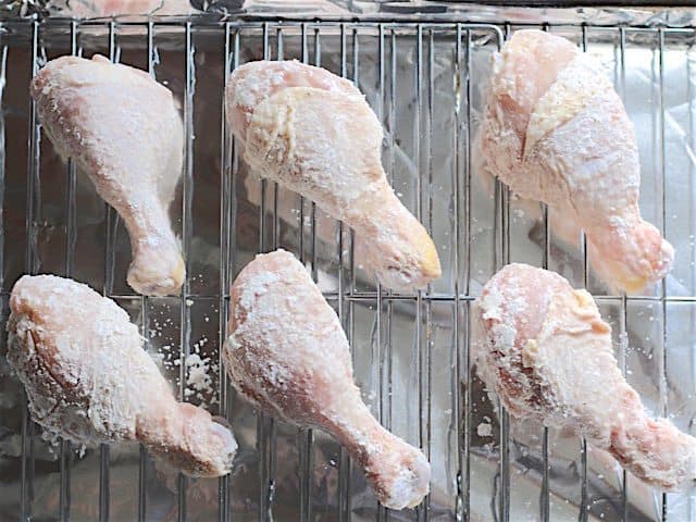 Coated drumsticks on a wire rack lined baking sheet ready to bake