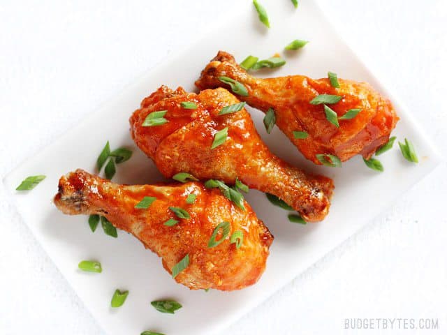 Sweet and spicy honey sriracha chicken drumsticks baked to perfection in the oven! Change up the sauce for a different meal every week! BudgetBytes.com Overhead view of three Crispy Baked Honey Sriracha Chicken Drumsticks on a plate