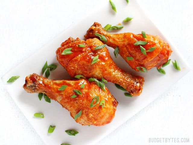 Overhead view of three Crispy Baked Honey Sriracha Chicken Drumsticks on a plate