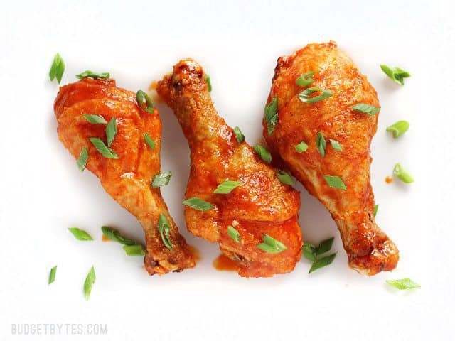 Three Crispy Baked Honey Sriracha Chicken Drumsticks on a white plate, garnished with green onion