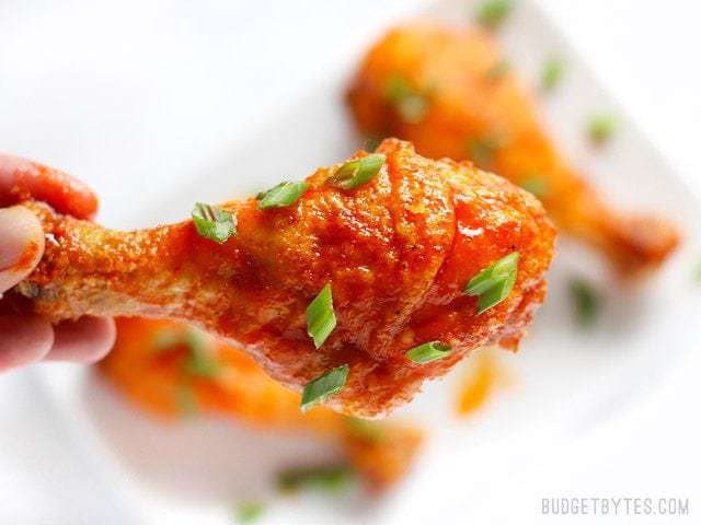 One honey sriracha baked drumstick held close to the camera, garnished with green onions
