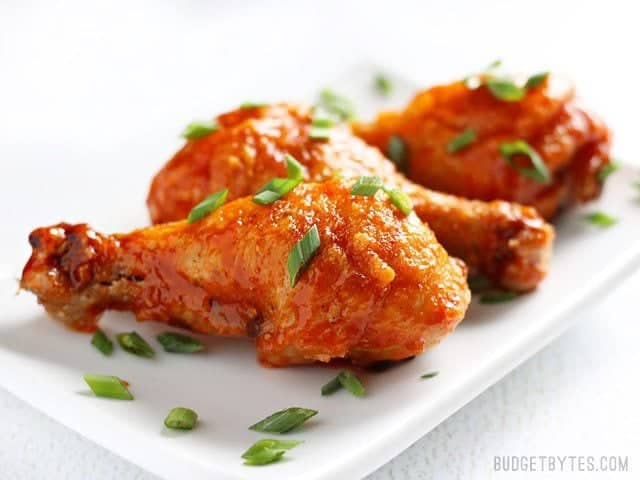 Side view of Crispy Baked Honey Sriracha Chicken Drumsticks on a white rectangular plate