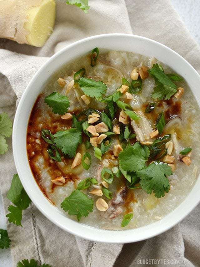 Overhead view of a bowl of congee topped with soy sauce, sesame oil, peanuts, and cilantro.