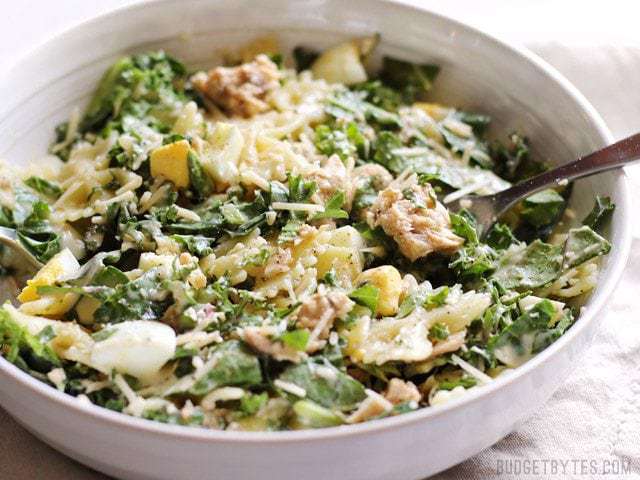 Side view of a white bowl with kale and salmon caesar salad, with eggs and bowtie pasta. 