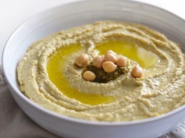 Close up side view of a bowl of Pesto Hummus garnished with oil, pesto, and chickpeas