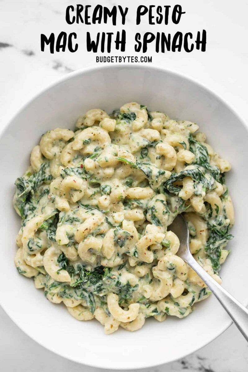 Overhead view of a bowl of creamy pesto mac with spinach, title text at the top
