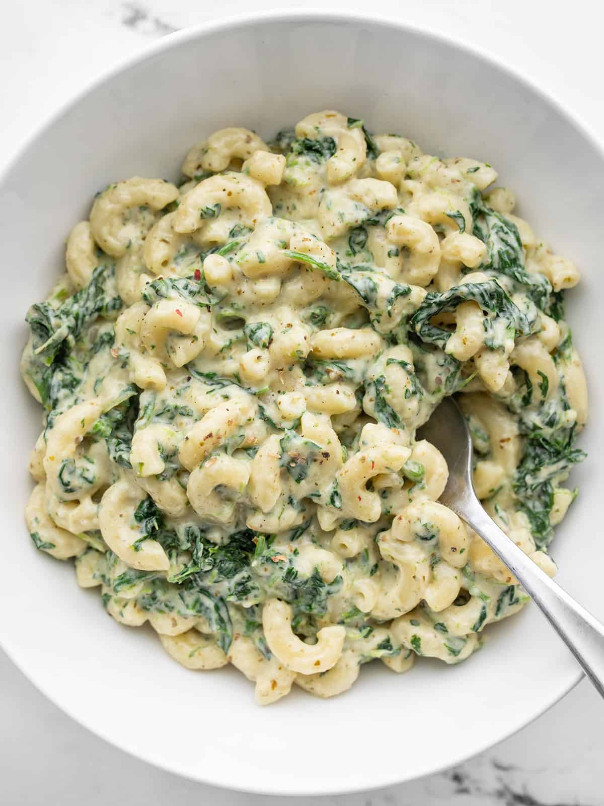 Close up overhead view of a bowl of creamy pesto mac with spinach, fork in the center