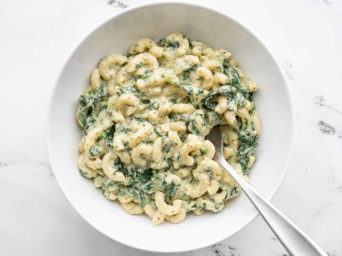 Overhead view of a bowl full of creamy pesto mac with spinach, a fork in the center