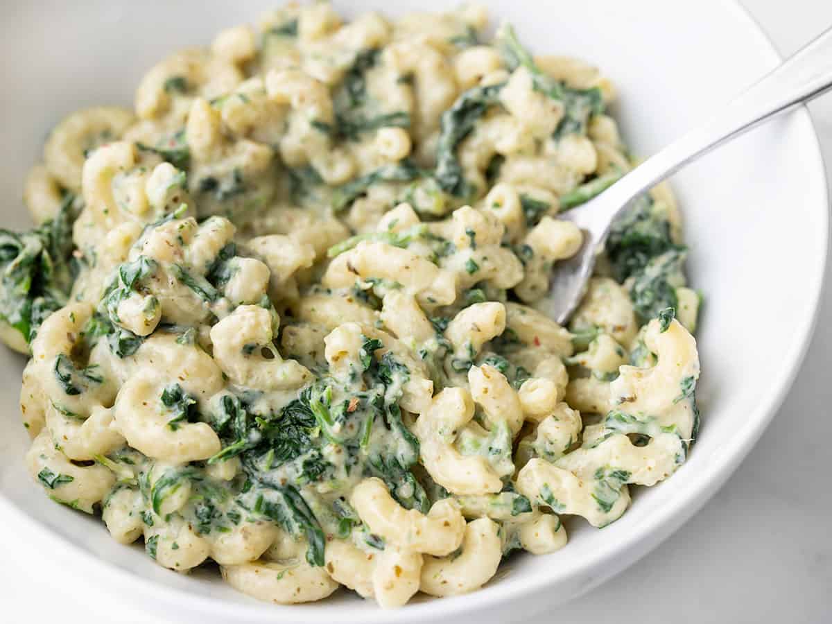 Close up side view of a bowl of creamy pesto mac with spinach