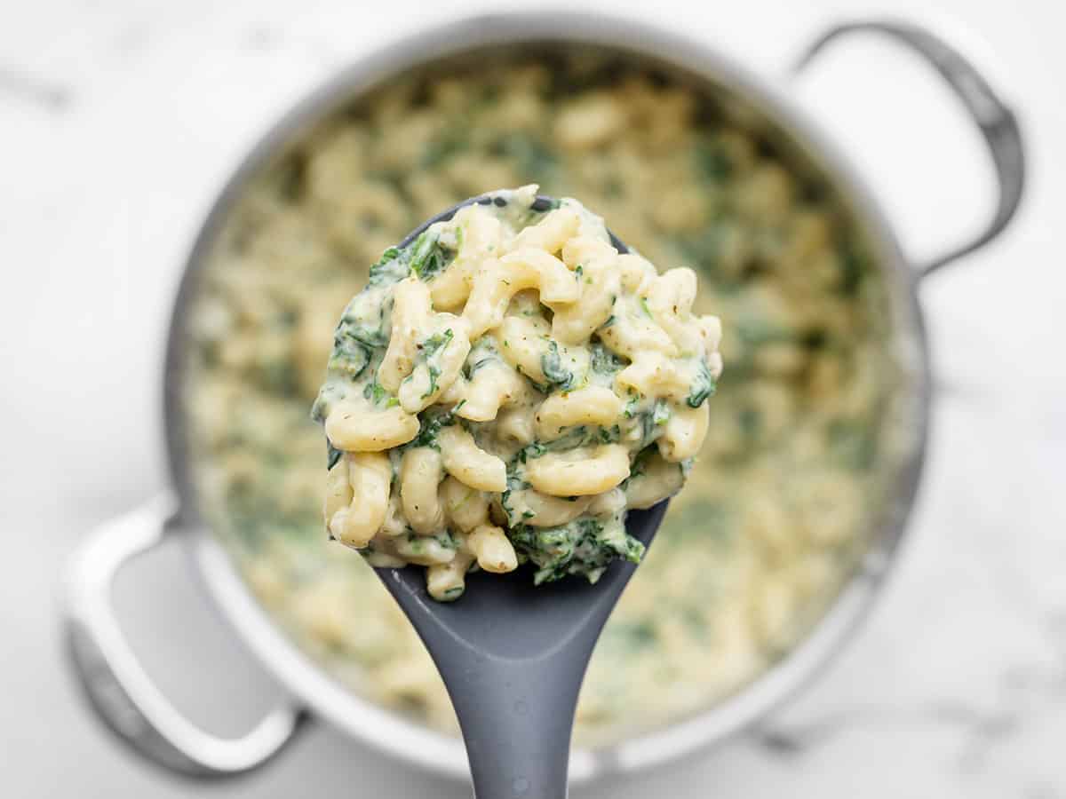 Close up of a spoonful of creamy pesto mac with the pot in the background