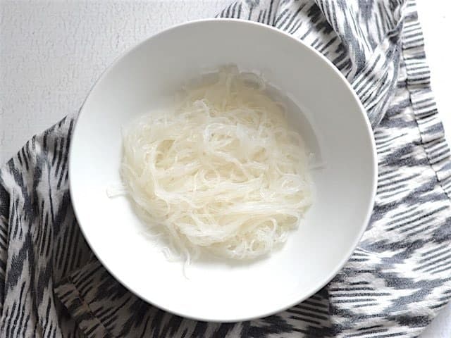 cooked noodles in a bowl alone, sitting on a striped napkin.