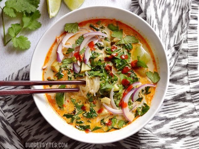 Thai Curry Vegetable Soup sitting on a striped napkin, being eaten with a pair of wooden chopsticks.