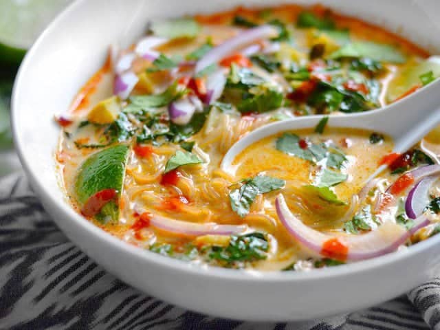 Close up of a ceramic spoon in a fully garnished bowl of Thai Curry Vegetable Soup 