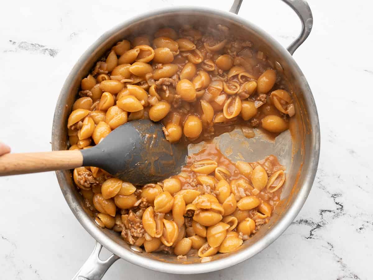 Cooked pasta in the skillet a spatula pulling the pasta aside to show the sauce