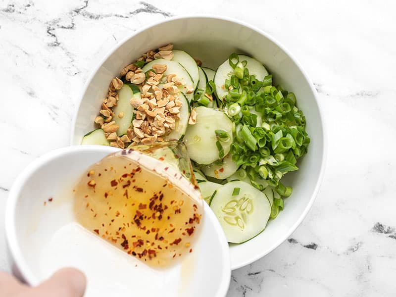 Dressing being poured over cucumbers, green onion, and peanuts