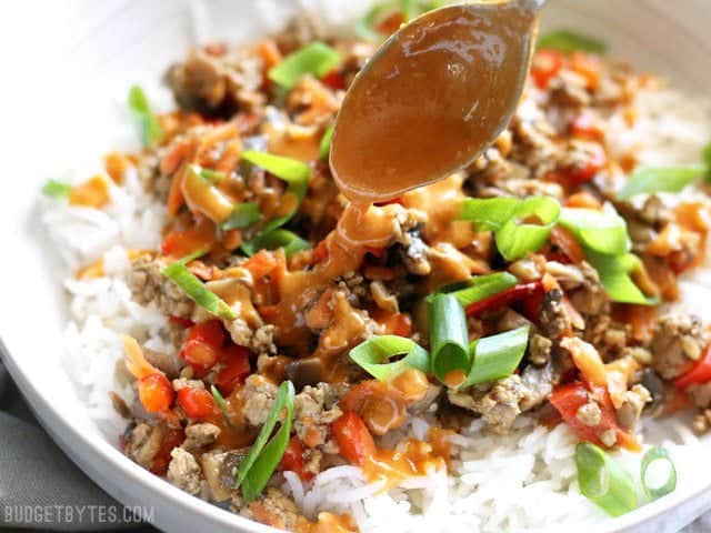 Spicy peanut sauce being drizzled over a hoisin stir fry bowl