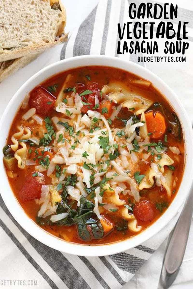 Overhead view of a bowl full of Garden Vegetable Lasagna Soup with bread on the side, title text at top