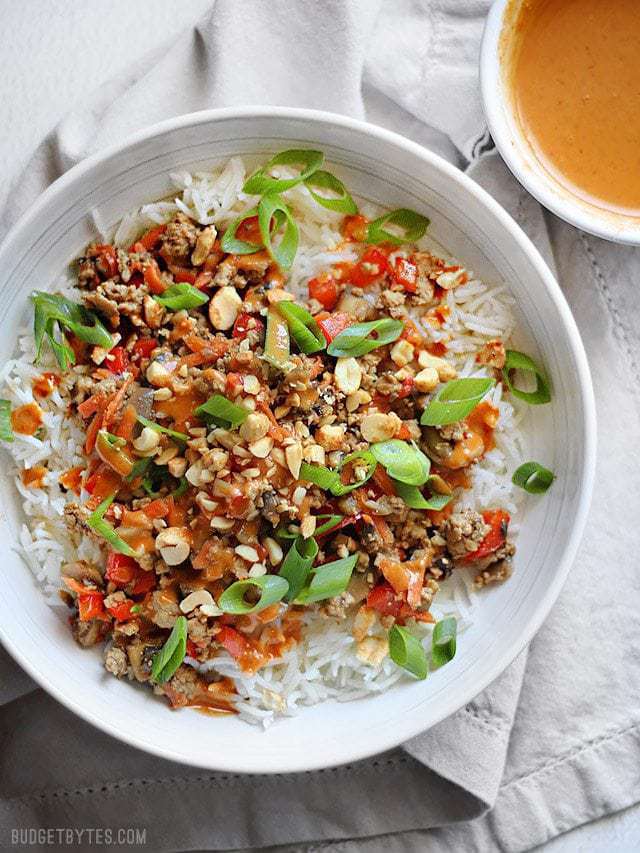 Overhead view of a hoisin stir fry served over rice with a smaller bowl of peanut sauce on the side