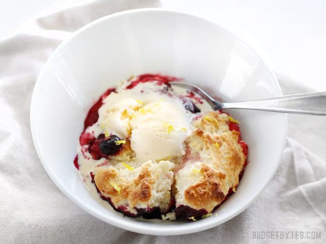 Lemon Berry Cobbler in a bowl with ice cream being eaten with a spoon
