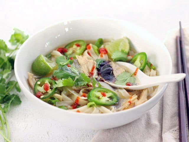 Quickie Faux Phớ is the next best to the real thing when you're short on time. Hot broth, tender noodles, shredded chicken, and tons of fresh toppings! BudgetBytes.com Front view of a bowl of Quickie Faux Phở with a spoon in the middle