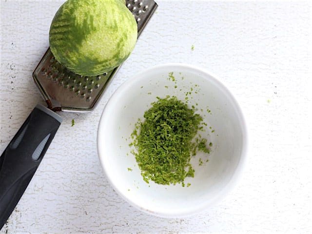 Zested Lime sitting on a microplane with a bowl of lime zest on the side