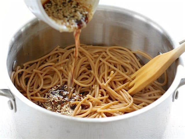 Sesame dressing being poured onto cooked pasta in the pot