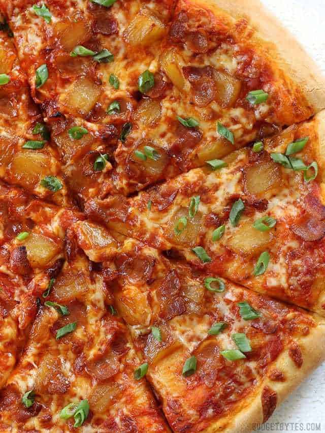 Close up overhead view of a sliced Bacon Pizza with caramelized pineapple and green onion