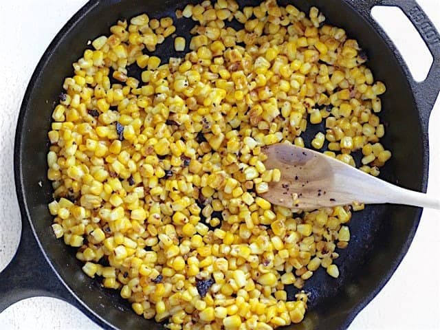 Blackened Corn in a cast iron skillet with a wooden spoon