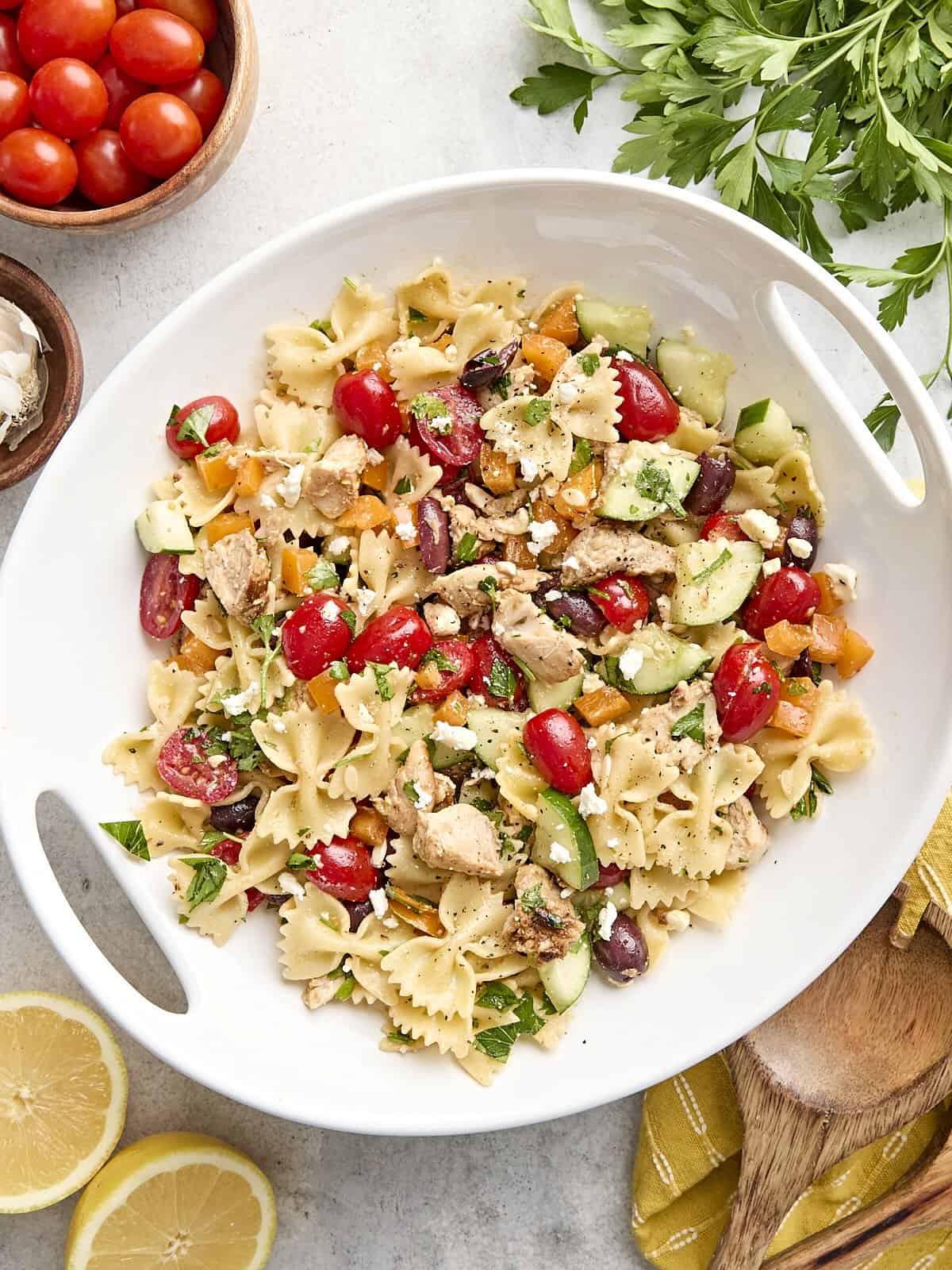 Greek Chicken Pasta Salad is the perfectly refreshing and filling summer meal with its medley of vegetables and tangy lemon garlic dressing. BudgetBytes.com Overhead view of a homemade Greek chicken pasta salad on a platter.