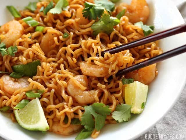 Close up of Lime Shrimp Dragon Noodles in the bowl with chopsticks picking up a piece of shrimp and some noodles
