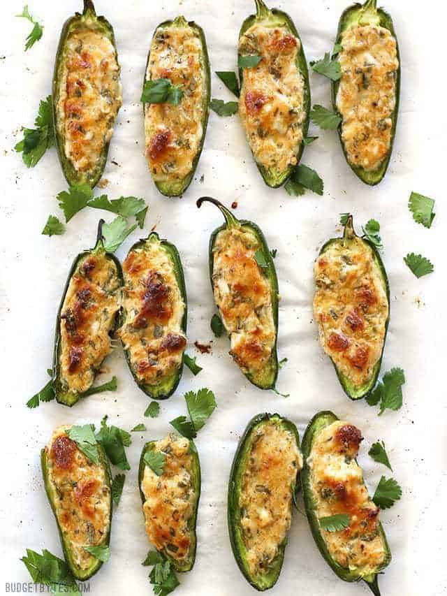Cheesy Scallion Stuffed Jalapeños are a quick, easy, and impressive appetizer for your game day get together or any party platter! BudgetBytes.com Stuffed Jalapeños viewed from above lined up on a piece of parchment paper, garnished with cilantro