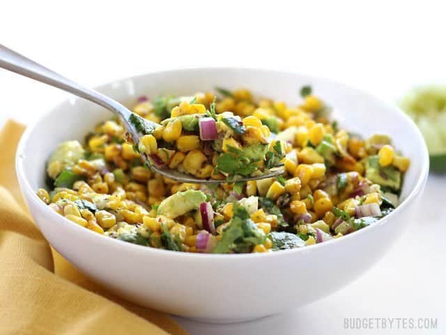 Front view of a bowl full of Warm Corn and Avocado Salad with a fork lifting a bite