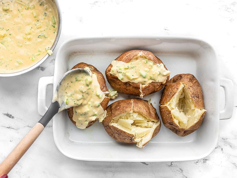 Broccoli cheese sauce being spooned onto baked potatoes