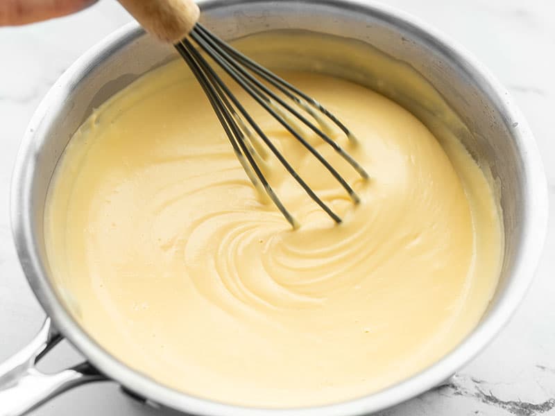A whisk stirring the thickened cheese sauce