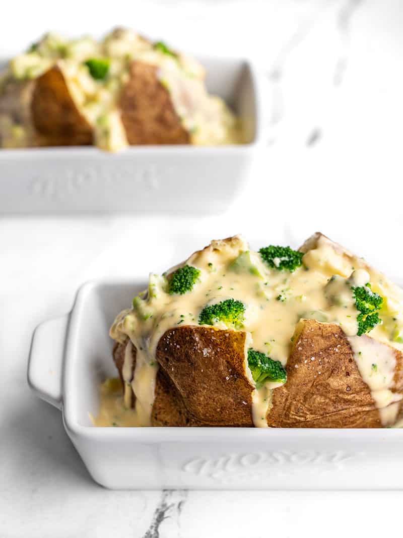 Two broccoli cheddar stuffed potatoes, each in an individual white casserole dish