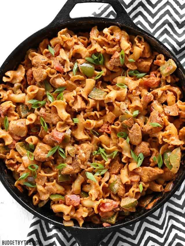 Creamy Chicken Fajita Pasta is a fast and delicious weeknight meal with spicy southwest flavors and a rich creamy sauce that the whole family will love. BudgetBytes.com Overhead view of a cast iron skillet full of Creamy Chicken Fajita Pasta on a zig zag black napkin