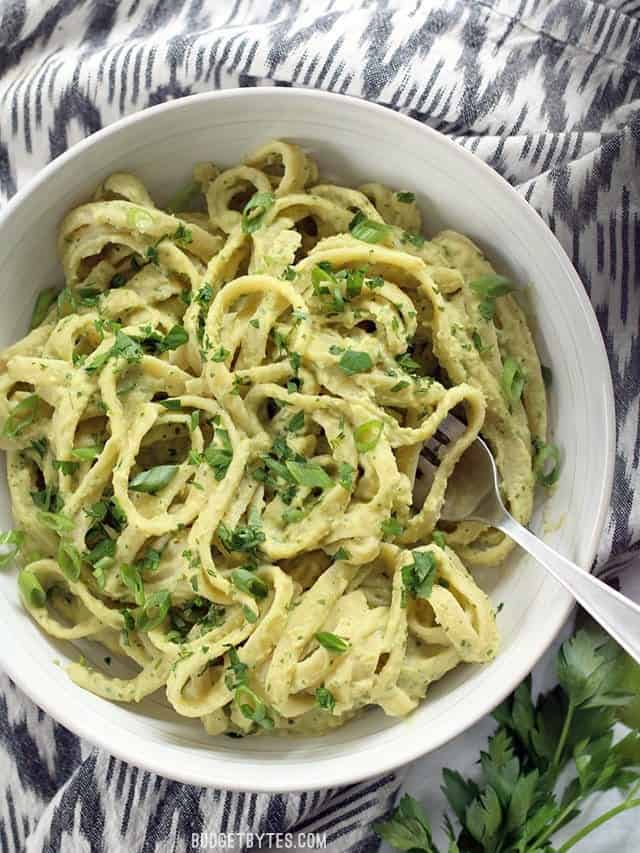 A big bowl of Parsley Scallion Hummus Pasta, garnished with fresh parsley, on a black and white ikat napkin.