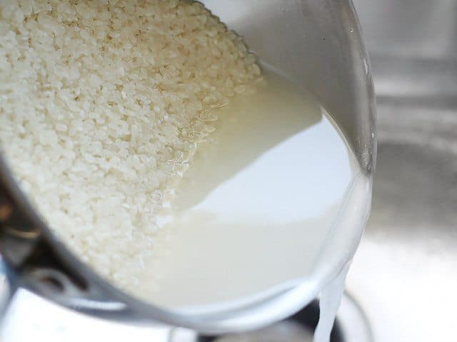 Rice being rinsed, cloudy water being poured off from the pot