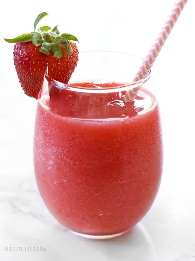 Front view of a short glass of Strawberry Rosé Slush with a fresh strawberry garnish and a pink striped paper straw